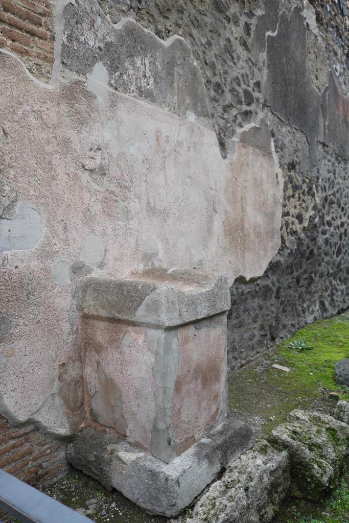Pompeii street altar on west side wall of I.11.1. May 2006. 
Remains of painting above altar. The right hand Lar can be seen with his left hand raised holding a cornucopia. A curving line flows from the cornucopia, above his head and down to the situla (bucket) in his right hand. The curve of the serpent can be seen above the top of the painted round altar. 
The head is down to the left reaching into the burning offering on the top of the altar.  The garland can be seen above the Lar.

