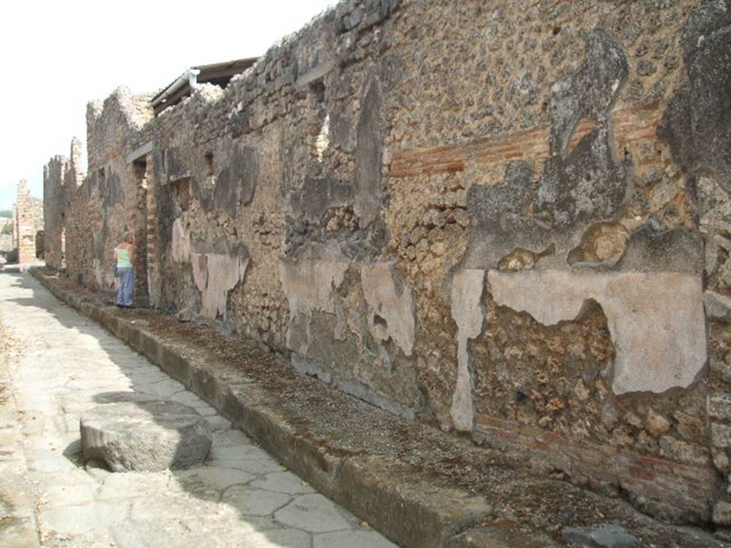 Vicolo di Tesmo looking north past remaining painted plaster on walls outside IX.7.20.
On the exterior wall of IX.7.20, opposite the doorways of IX.2.17/18, a large painted lararium was found.
According to Trendelenburg, this stood out because of the freshness and strength of the colours.
It was divided into two parts, of differing sizes. The upper part was 1.47m wide and the lower part was 4.12m wide.
The upper part showed the two Lares.
In the middle between them was the Genius with cornucopia, dressed in a white tunic holding a patera above a flaming altar. 
Behind the altar was the figure of small tibicen who played the double pipes. 
Suspended above were two garlands and above the garlands appeared the bust of Luna on the left and a bust of Sole on the right. 
The lower part showed a tall altar in the centre and three heads of Medusa. 
Two serpents approached the altar, one from each side.
See Trendelenburg in BdI 1871, pp. 199-200.
See Sogliano, A., 1879. Le pitture murali campane scoverte negli anni 1867-79. Napoli: Giannini. (p.14, No. 33).
See Fr�hlich, T., 1991. Lararien und Fassadenbilder in den Vesuvst�dten. Mainz: von Zabern. (F65, p. 335)
