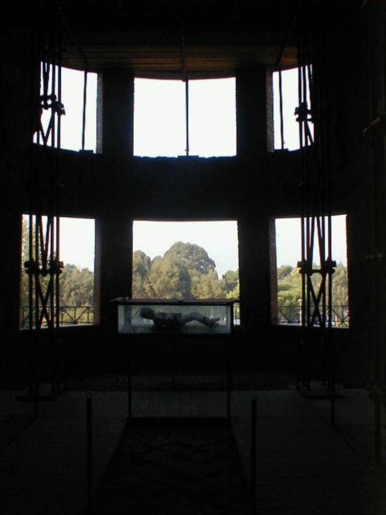 VII.16.17-22 Pompeii. September 2004. Looking west towards curved apse with six windows, in oecus.
A plaster cast of victim 48, is on display in the case.