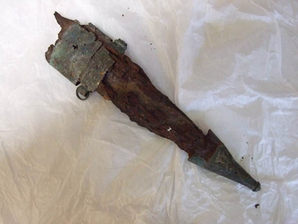Nola Gate, Pompeii, March 2009. View from above. Large iron knife in a bronze and wooden sheath.
Found near Porta Nola in 1976. SAP inventory number 17047.
Man no. 5 had on the left a sheathed dagger (fig. 27) and the scabbard (fig. 28) empty of a second smaller blade: at the feet shoes with a nailed sole.
See De Caro S., 1976. Scavi nell’area fuori Porta Nola a Pompei: Cronache Pompeiane V, p. 99, fig. 27.