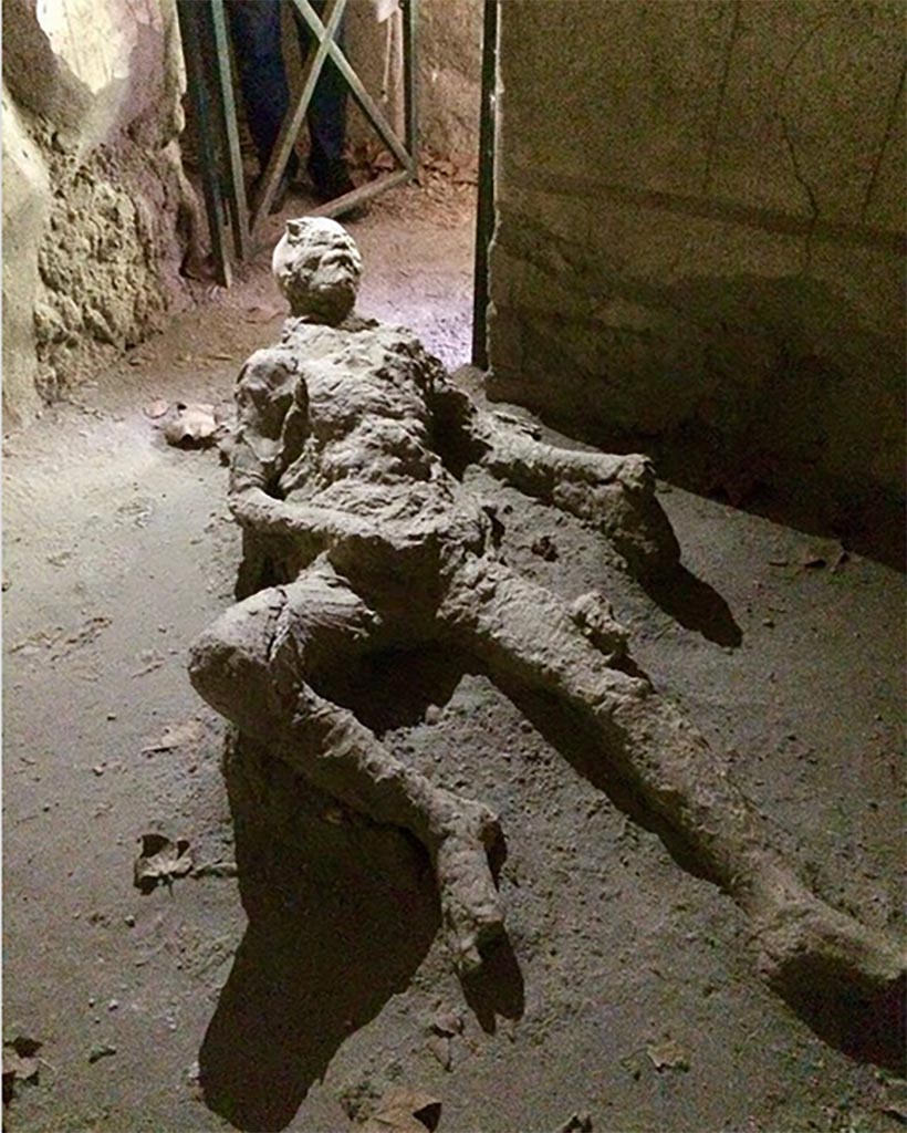 Victim 67. Male victim aged over 20 years. 
Photograph © Parco Archeologico di Pompei.
Found in room 28 of VII.16.17 Casa di Maius Castricius between 1958 and 1980.
Traces of fabric are recognizable especially on the right shoulder and legs. 
He was probably wearing a short tunic with three-quarter sleeves. 
On the right tibia there are traces of fabric perhaps belonging to a bandage to plug a wound.
The position has always remained the same, that is, room 28 of VII.16.17 Casa di Maius Castricius.
See Osanna, N., Capurso, A., e Masseroli, S. M., 2021. I Calchi di Pompei da Giuseppe Fiorelli ad oggi: Studi e Ricerche del PAP 46, p. 476-7, Calco n. 67.
The victim was found in the southwest corner of room 28.
See Varriale I., 2006. in Aoyagi M. and Pappalardo U., 2006. Pompei (Regiones VI-VII) Insula Occidentalis. Napoli: Valtrend, p. 476.

