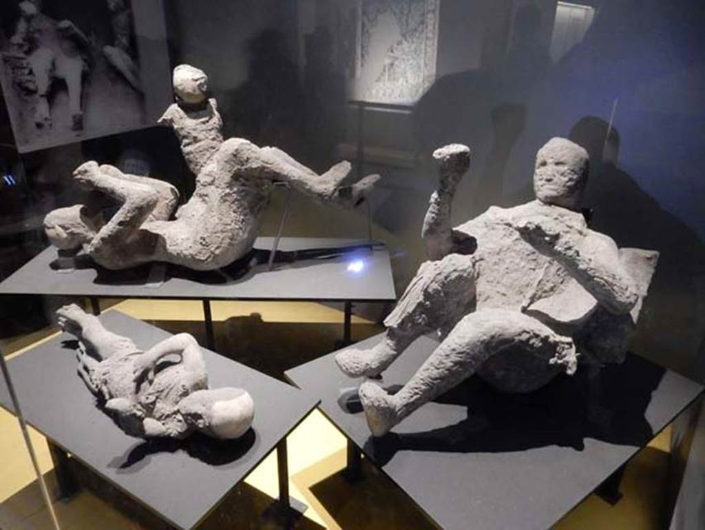 VI.17.42 Pompeii. Victims 50 to 53, May 2018.
Plaster casts of fugitives found in the lower corridor, see VI.17.42, Lower and Garden, for area. Photo courtesy of Buzz Ferebee.
Experts had previously made assumptions about the victims' identities and relationships, but new DNA evidence counteracts their long-held theories.
Inside the House of the Golden Bracelet, three people were discovered at the foot of the staircase - the location gets its name from the jewellery one of the two adults was wearing. This, in addition to the adult being found with a child on their hip, caused experts to believe this victim was a mother of two and the father was the second adult.
But this isn't the case, according to scientists in Italy, Germany and the US as written in the Current Biology journal 2024, as the victim sporting the bracelet was actually found to be a dark-haired, dark-skinned male and he has no relation to the two infant boys found with him, while genetic evidence also appears to point to the second adult also being a male too.
Meanwhile, all three had various eastern Mediterranean or North African origins.
Andrew Wallace-Hadrill, a professor at the University of Cambridge who wasn't involved in study noted how this new DNA evidence "turns some older interpretations, especially those based on rather romantic assumptions, on their head".
He also commented on how this evidence reflects the society at the time.
"One would predict, in a society heavily based on slavery, a significant diversity."
“It is very interesting for instance they have identified an individual with dark skin and black hair, which strongly points to an enslaved person from Africa.”