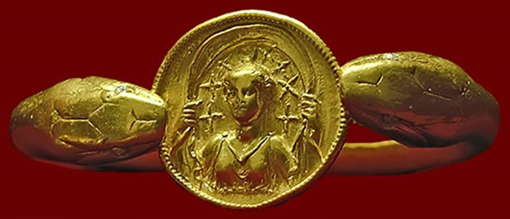 VI.17.42 Pompeii. Golden bracelet found on the arm of a woman.
According to Barbara McManus, this remarkable bracelet, 610 grams (21.5 oz) of solid gold, is fashioned in the form of two snakes flanking a round disk with a carved relief of Selene with crescent moon and stars above her head.
It was found on the arm of a woman carrying a casket containing 40 aurei and 180 denarii.
She was killed along with another adult and a child when a balcony collapsed in the house.
Photo courtesy of Barbara McManus. See The VRoma Project
Now in Naples Archaeological Museum. Inventory number 14268.
According to recent DNA analysis in 2024, the victim sporting the bracelet was actually found to be a dark-haired, dark-skinned male and he has no relation to the two infant boys found with him.