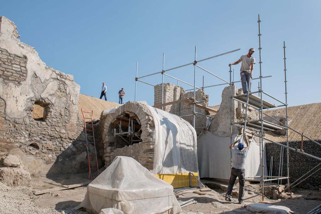 Pompeii Fountain at V.8 during excavation.
Looking north-east from crossroads on Vicolo delle Nozze d’Argento, towards a small square/open area with water tower at rear, well/cistern with arched roof and fountain (covered).
The gladiator fresco is on the back of the wall to the right of the water tower and behind the well/cistern.
Fontana di Pompei a V.8 durante lo scavo. Quadrivio con torre d'acqua sul retro, pozzo/cisterna con tetto ad arco e fontana (coperta).
L'affresco gladiatore si trova sul retro della parete a destra della torre dell'acqua e dietro il pozzo/cisterna.
Photograph © Parco Archeologico di Pompei.