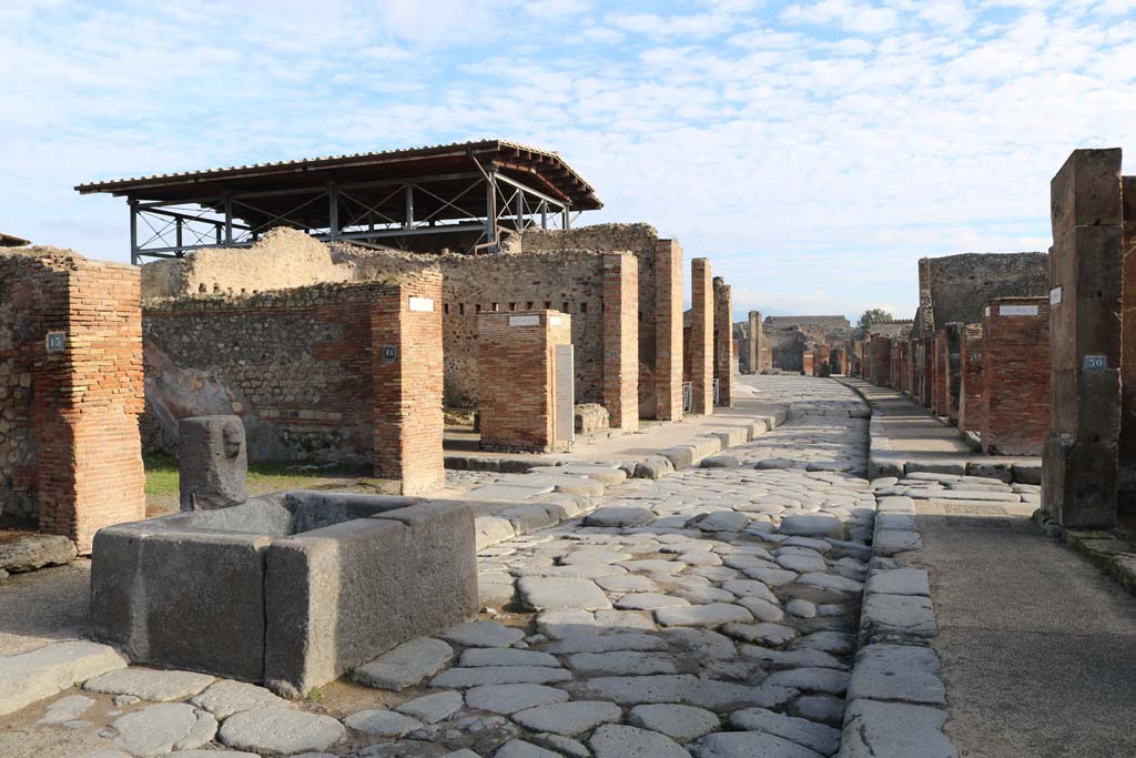 Fountain outside VII.14.13 and VII.14.14 on Via dell�Abbondanza, Pompeii. December 2018. 
Looking east from fountain towards junction of Vicolo del Lupanare, on left, and Via dei Teatri, on right. 
Photo courtesy of Aude Durand.

