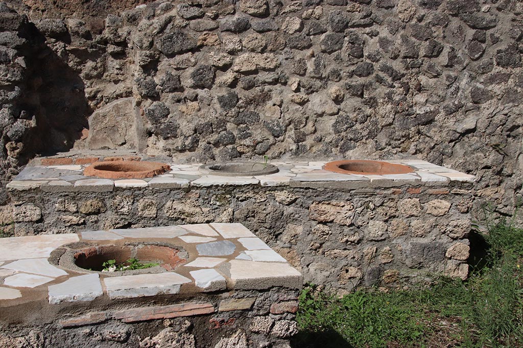 I.2.8 Pompeii. October 2024.
North wall with niche behind additional counter with three urns, and L-shaped serving counter at the front. Photo courtesy of Klaus Heese.