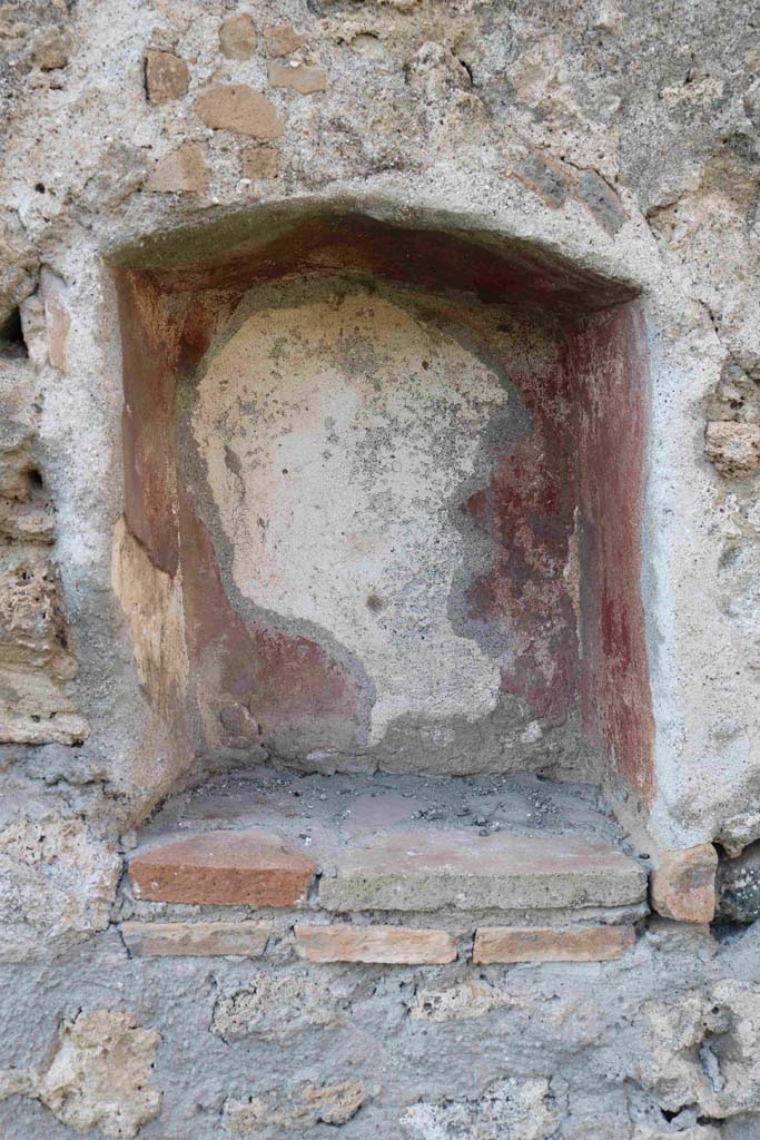 I.2.22 Pompeii. September 2018. Room 1, north wall with niche. Photo courtesy of Aude Durand.
According to Boyce –
In the room into which one enters directly from the street, in the north wall is an irregular rectangular niche (h.0.50, w.0.42, d.0.25, h. above floor 1.40) with peaked ceiling, its interior walls painted red.
See Boyce G. K., 1937. Corpus of the Lararia of Pompeii. Rome: MAAR 14. (p.23, no.14).