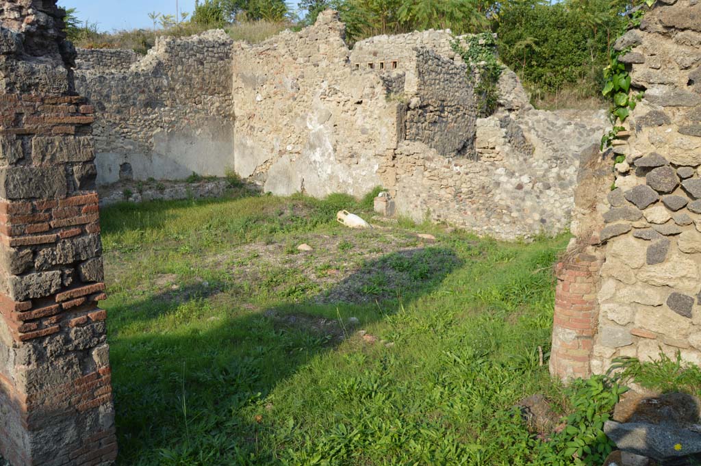 I.2.24 Pompeii. October 2017. Looking towards the north and east walls of the peristyle.
Foto Taylor Lauritsen, ERC Grant 681269 DÉCOR.
According to Boyce –
In the east wall of the peristyle, above one of the beds of a masonry triclinium, is a niche, described by Fiorelli as a sacrario, more fully by Mau as “un aedicula, una base, cioe, con una piccola tavola, che sta in un specie di nicchia coperta a volta, e probabilmente conteneva un’idolo”.
There remains now only the solid base (0.40 by 0.32, h.0.65) and on the wall above it the marks left by a vaulted structure which rested on the base.
He quotes references – Bull. Inst., 1874, 262; Fiorelli, Descr., 47.