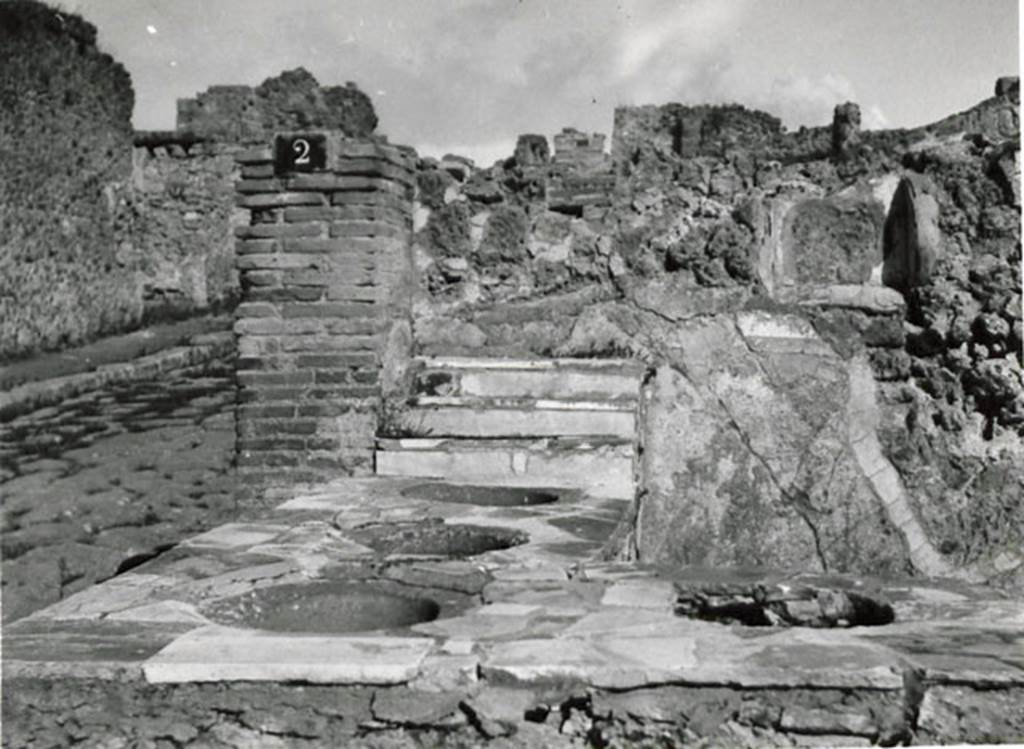 I.3.2 Pompeii. 1935 photograph by Tatiana Warscher. Looking north along west side of the counter showing four embedded dolia, with Via Stabiana on the left. The niche, as mentioned by Boyce above, can be seen in the north wall. According to Warscher, quoting Fiorelli – “I.3.2, Bottega con podio, in cui stanno infisse quattro grandi urne di terracotta, avendo a destra una gradinata. Nel muro nord si trovano i resti della nicchia dei penati”.
See Warscher, T, 1935: Codex Topographicus Pompejanus, Regio I, 3: (no. 3), Rome, DAIR, whose copyright it remains.
