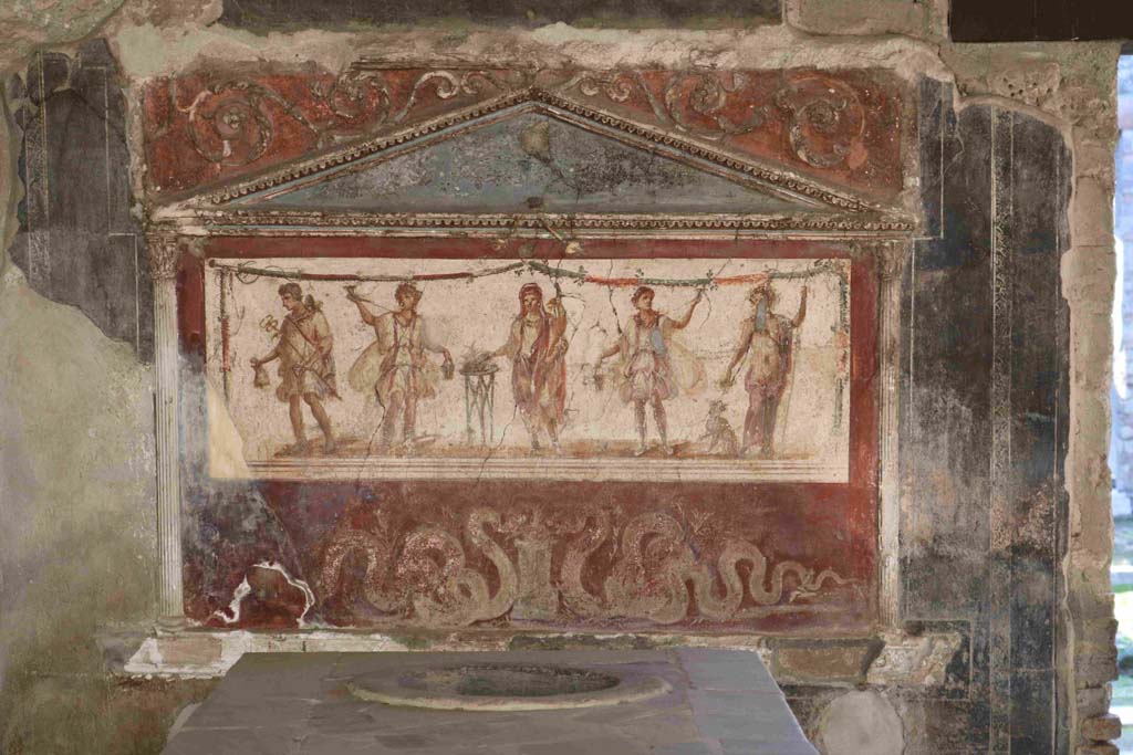 I.8.8 Pompeii. December 2018.Lararium on south wall. Photo courtesy of Aude Durand.
The central figure is the Genius of the household next to a three-legged altar.
On either side of him are the two Lares. On the left side is Mercury with his money bag.
On the right side is Bacchus with his panther drinking from a cup held in his right hand.
Underneath are two serpents approaching a round altar.
See Fröhlich, T., 1991, Lararien und Fassadenbilder in den Vesuvstädten. Mainz: von Zabern. (L8: p.252).