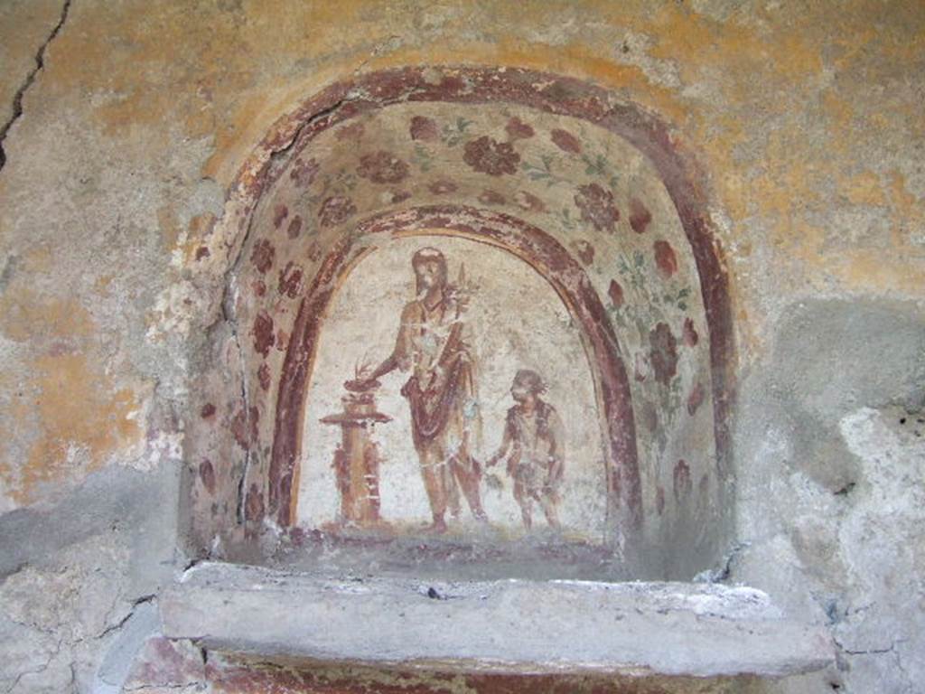 I.17.4 Pompeii. May 2006. West wall of peristyle garden. Lararium niche.
Genius with patera in right hand and cornucopia in the left hand is sacrificing at a round altar. A small child with a brocca or jug is on the left of the genius. See Bragantini, de Vos, Badoni, 1981. Pitture e Pavimenti di Pompei, Parte 1. Rome: ICCD. (p.204/5).