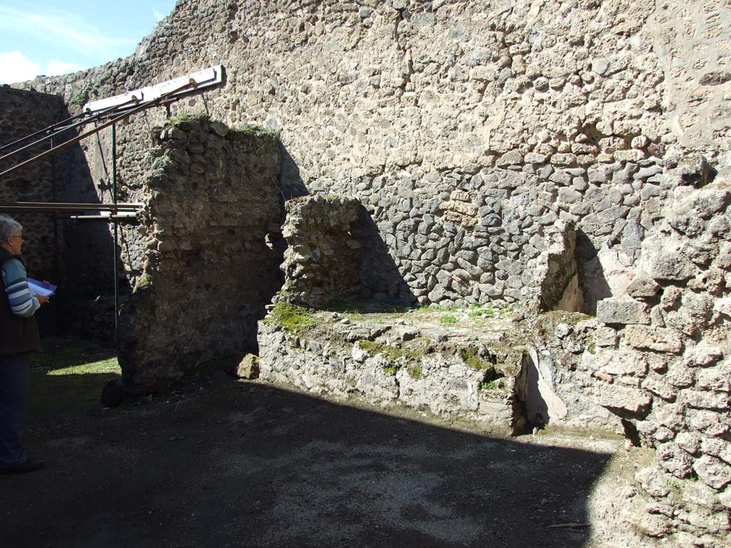 V.1.23 Pompeii. March 2009. Room “n”, north wall of kitchen area, with bench.
According to Boyce, in the kitchen on the wall at the side of the hearth was a lararium painting.
In the middle was an altar around which a serpent was coiling and on the right of it stood the Genius.
On the left stood a Lar, the second Lar stood behind the Genius.
Underneath there were another two serpents, further on the right side the figure of river Sarnus reclined, crowned with reeds and with a jar at his elbow.
The background was filled with plants.
See Boyce G. K., 1937. Corpus of the Lararia of Pompeii. Rome: MAAR 14. (p.32, no.79)
Nothing remains of the painted Lararium today.
Sogliano described the lararium and placed it at V.1.10, the kitchen at the rear entrance doorway.
In 1879, when his book was published, he described the lararium as a “representation of the Lares with Genius now destroyed, the plaster has fallen, and only the Sarnus figure remains sitting and crowned…..”.
See Sogliano, A., 1879. Le pitture murali campane scoverte negli anni 1867-79. Napoli: (p.15, no.37)
Sogliano quotes Bull.Inst.1876, p.246.