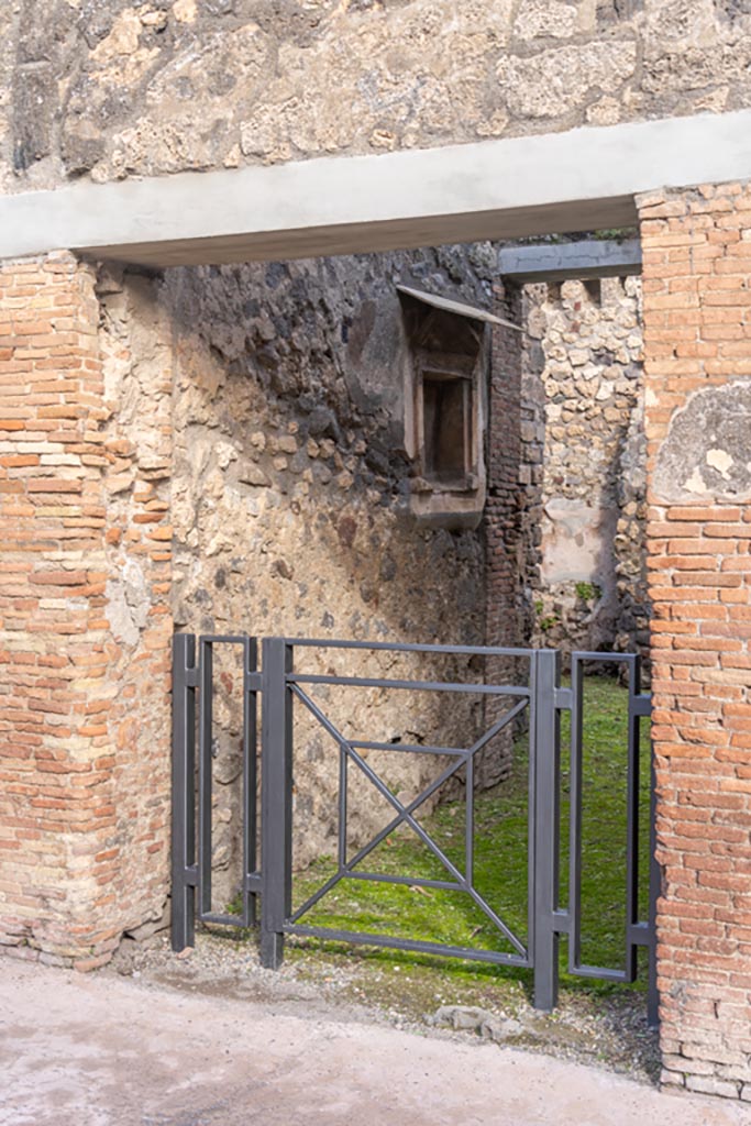 V.1.28 Pompeii. January 2024.
Looking towards north side of entrance fauces/corridor, with niche. Photo courtesy of Johannes Eber.
According to Boyce, the square niche was surrounded by an elaborate aedicula façade of stucco.
In the floor of the niche were holes for the bases of statuettes.
The niche and façade were brightly coloured, the rear wall was white bordered with red and having delicate painted green plants on it.
The pilasters of the façade were yellow, their capitals red, white and blue.
The bands of relief that ran around the architrave and the cornices were also painted in these colours.
On the wall below the niche was a painted band of yellow.
See Boyce G. K., 1937. Corpus of the Lararia of Pompeii. Rome: MAAR 14. (p.33, no.81, and Pl.1,5)
Described by Giacobello as a Pseudo-aedicula lararium.
See Giacobello, F., 2008. Larari Pompeiani: Iconografia e culto dei Lari in ambito domestico. Milano: LED Edizioni, (p.231, no.F4)
