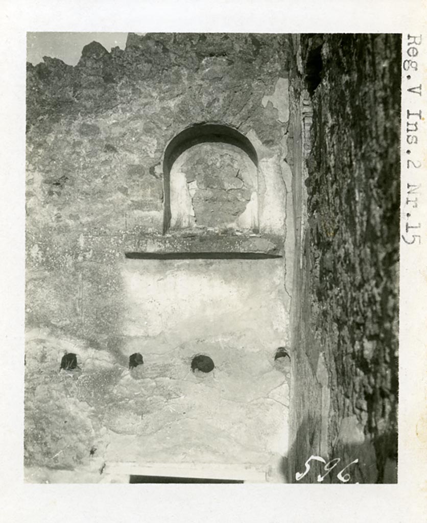 V.2.d Pompeii but shown as V.2.15 on the photo. Pre-1937-39. Niche “n” on plan.
Looking towards vaulted niche lararium on upper north wall, in north-east corner of rear of house.
Photo courtesy of American Academy in Rome, Photographic Archive. Warsher collection no. 596
According to Boyce, there were two lararia in the house.
One on the north wall of a rear room that occupied the place of the peristyle, high above the floor, was a large arched niche (0.8m high, 0.65m wide, 0.35m deep, 2.9m high above the floor) with a heavy projecting ledge beneath it.
Painted on the back wall of this niche, was a burning altar adorned with a garland and furnished with two eggs, and on each side of the altar was a palm branch, yellow with red ribbon attached.
The wall around the niche was covered with white stucco which below the niche was studded with red spots representing a dado, down as far as a row of holes, where a kind of mezzanine was attached, by means of which the niche was reached.
At a late date this structure was removed and Mau supposed that the niche was reached thereafter by a portable ladder.
See Boyce G. K., 1937. Corpus of the Lararia of Pompeii. Rome: MAAR 14. (p.36, nos.101 and 102,)
See Bullettino dell’Instituto di Corrispondenza Archeologica (DAIR), 1885, p.256.
According to PPM, nothing remains of the painting other than a small amount of the base stucco.