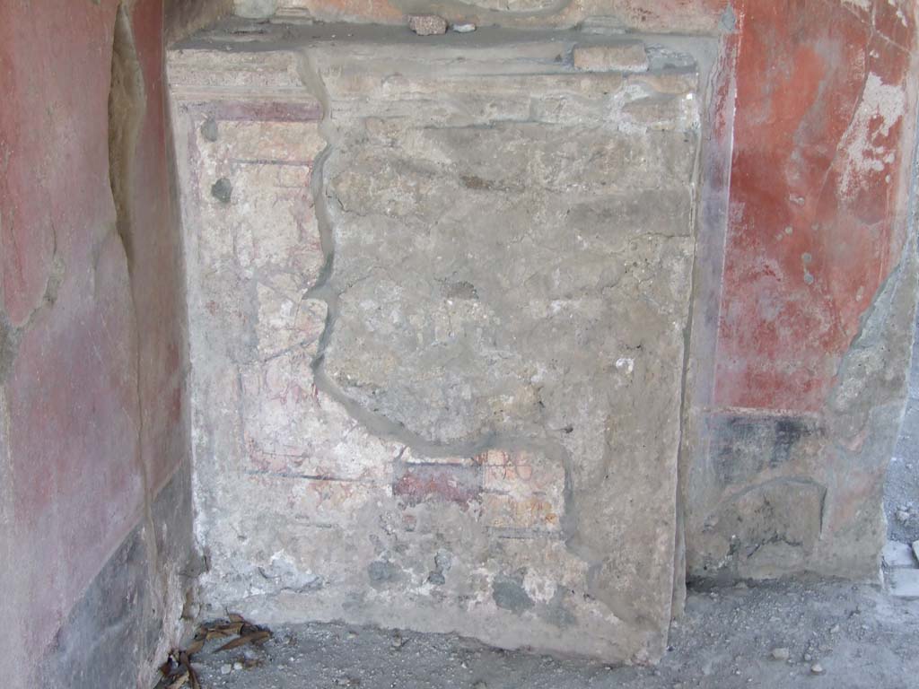 V.3.4 Pompeii. March 2009. Podium base of lararium. The podium was covered in stucco painted to look like red marble with insets.
The insets were of red rectangles and yellow diamonds with a large green slab in the centre of the two free sides.
The slab on the south side was circular whilst that on the east was diamond shaped.
A stucco cornice in red, white and blue runs along the top of the base.
See Boyce G. K., 1937. Corpus of the Lararia of Pompeii. Rome: MAAR 14. (p. 38, 111, Pl 38,1).