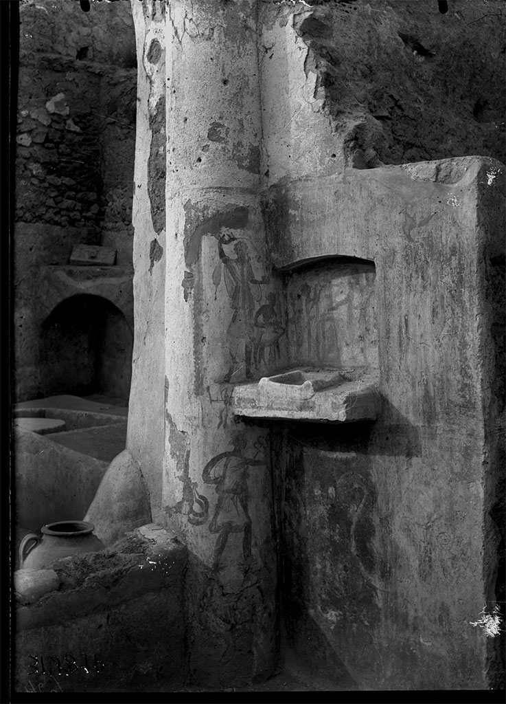 V.4.b Pompeii. 1931. Lararium found on the east wall of the atrium, near the kitchen door.
DAIR 31.2876. Photo © Deutsches Archäologisches Institut, Abteilung Rom, Arkiv.
A heavy shelf with a low raised area for a built-in altar projects from a niche with a slightly arched ceiling.
Within the niche was a crudely done lararium painting on a yellow background.
Above and to the sides hung garlands.
On the back wall of the niche the Genius pours a libation upon a cylindrical altar, on the opposite side of which stands the tibicen.
On the wall outside the niche is a Lar on each side, the one on the right holding rhyton and situla, that on the left rhyton and a cup like a skyphos.
On the left side wall of the niche, between the Lar on that side and the back wall of the niche, is the popa leading a hog.
Below the level of the niche on the left side, is Mercury with petasos, caduceus and purse; behind him, suspended, two crescent-shaped objects.
These three figures on the left side are painted on the column of the peristyle in the south-east corner of the garden.
Immediately below the niche a crested serpent (two serpents according to Sogliano in the Not. Scavi, one according to Mau in the Rom. Mitt.) glides to the left among plants.
See Boyce G. K., 1937. Corpus of the Lararia of Pompeii. Rome: MAAR 14. (p.42, no.129, Pl 13,1)
See Jashemski, W. F., 1993. The Gardens of Pompeii, Volume II: Appendices. New York: Caratzas, p. 117
See Giacobello, F., 2008. Larari Pompeiani: Iconografia e culto dei Lari in ambito domestico. Milano: LED Edizioni, p.168.