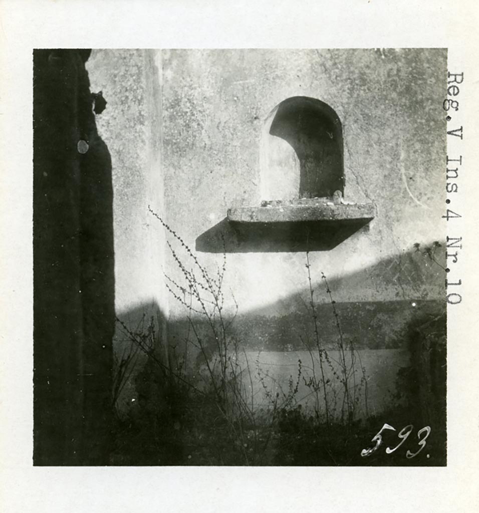 V.4.c Pompeii but shown as V.4.10 on photo, 1937 or earlier, by Tatiana Warscher. Niche lararium (e) in east wall of garden K.
Photo courtesy of American Academy in Rome, Photographic Archive. Warsher collection no. 593.
According to Boyce, this niche was placed at the east end of the corridor leading from the atrium.
The arched niche had a heavy ledge projecting from the wall.
Upon this ledge was placed an ordinary roof tile, the raised edges of which, when covered with stucco would look like an altar.
The rear wall was painted blue or green, and painted with plants.
Boyce was not sure if this was a Lararium, but he thought as there was no other Lararium in the house, it may possibly have been one.
He said that Sogliano attached religious importance to a painting of Mercury found on the east wall of the atrium.
See Notizie degli Scavi di Antichità, 1905, p. 131.
See Boyce G. K., 1937. Corpus of the Lararia of Pompeii. Rome: MAAR 14. (p.42, no.130, Pl. 3,1 - which is this photo by Warscher)
In a note on page 42, Boyce added that a collection of items were found, perhaps, gathered together for flight.
Included were a glazed terracotta statuette of Harpocrates and a small terracotta altar.
See Bullettino dell’Instituto di Corrispondenza Archeologica (DAIR), xvi, 1901, 364.