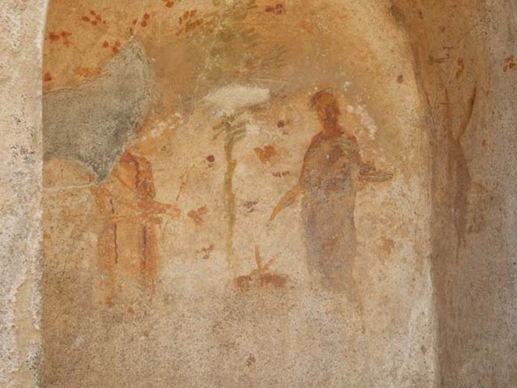 VII.1.46 Pompeii. May 2017. Room 14. Detail of niche lararium.
Photo courtesy of Buzz Ferebee.
According to Fröhlich, there was a painted wall surface with an arched niche on a white ground.
The inside of the niche was moderately to severely faded, especially on the side walls and the bottom of the rear panel.
On the back wall of the niche, on the right, stands Vesta in long purple robe, crowned, sacrificing on a round altar to her right.
On the right side panel a devoted donkey is facing the goddess.
Left of the altar is Vulcan, wearing a yellow robe, his right hand outstretched to the altar holding a pair of tongs and in the left a hammer.
On his head, the God wore a felt hat.
A green pine tree behind the altar occupies the centre of the image.
The background of the rear wall and the side walls and the ceiling is decorated with rough, red and green flowers.
The paintings outside the niche were destroyed.
Outside the niche were once left and right the flanking Lares in green tunics and blue cloaks, with Rhyton with Patera.
Below the niche was painted a ham, a pig's head and a meat skewer and a snake creeping to the right.
See Fröhlich, T., 1991. Lararien und Fassadenbilder in den Vesuvstädten. Mainz: von Zabern, L79, p. 282 and Taf. 40.2.