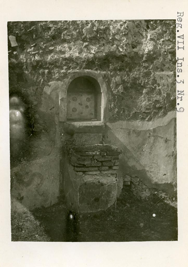 VII.3.8 Pompeii but shown as VII.3.9 on photo.
1930s photo by Tatiana Warscher. Room “c”, west wall. Lararium and altar.
Photo courtesy of American Academy in Rome, Photographic Archive. Warsher collection no. 587.
According to Boyce –
“Against the W. wall of the central room of the dwelling quarters stands a masonry altar (0.45 by 0.50, h. 0.75), coated with yellow stucco and having the two serpents painted on the wall, one on each side of it. In the wall above the altar is an arched niche (h. 0.54, w. 0,47, d. 0.17, b. above the floor 1.0), its inside walls coated with red stucco, upon which the attributes of Hercules - a club and a skyphos twined with laurel - are reported to have been painted. The niche today shows a coating with white stucco bordered with red stripes, and upon it are painted realistic red roses. On the wall above the niche was the ordinary lararium painting of the Genius in white toga with cornucopia and patera and on each side of him a Lar. The background was richly decorated throughout: in the upper panel beside the Lares were plants and birds, on the interior of the niche were red roses, around the serpents were plants and flowers. A small panel between the top of the altar and the ledge projecting below the niche was painted in imitation of coloured marble.
Fiorelli states in the Scavi that the niche perhaps contained a statuette of Hercules, in the Descr. that it did contain such a statuette; the report in the Bull. Inst. mentions no statuette.
See Boyce G. K., 1937. Corpus of the Lararia of Pompeii. Rome: MAAR 14. (p.63-4, Pl.12,1).