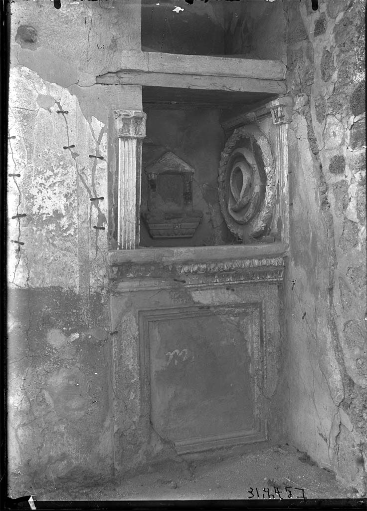 VII.3.13 Pompeii. Lararium on north wall of garden.
DAIR 31.2457. Photo © Deutsches Archäologisches Institut, Abteilung Rom, Arkiv.
According to Boyce, in the N. wall of the viridarium, to the left of the entrance door, a deep, square niche (0.84 square, d. 0,82, h. above the floor 1.15) is set in the wall.
Its floor projects slightly in the form of a ledge and beneath it runs a delicate cornice of modelled and painted stucco.
On the wall below the niche a rectangular panel is marked off by a moulding which runs around all four sides.
The side walls of the niche are adorned at their outer edges, each with a stucco pilaster fitted with curious capitals, one higher than the other.
In the centre of the back wall is a small aedicula facade formed by two columns (h. 0.25) which rest upon a heavy projecting ledge adorned with a cornice of stucco and support a pediment.
The back wall within the aedicula is painted in imitation of marble.
In this miniature shrine must have stood a statuette.
On the right side wall of the niche is a large wreath (diam. 0.70) of laurel and within it coils a serpent, all done in stucco relief.
Around the top of the three inside walls of the niche runs another stucco cornice.
In the floor is a rectangular depression for offerings.
This shrine was called the "Double Lararium", because above the niche we have described there is another, similar to it in shape and size.
But in this upper niche no traces of a cult were found and, in the absence of any real parallels to such a double shrine, it is simpler to regard the upper niche as a place of storage, comparable, perhaps, to the niches in the bases of the aediculae of the houses of Obellius Firmus and the Principe di Napoli (Nos. 67, 214).
See Boyce G. K., 1937. Corpus of the Lararia of Pompeii. Rome: MAAR 14, p. 64, no. 266, pl. 32,1.
See Giacobello, F., 2008. Larari Pompeiani: Iconografia e culto dei Lari in ambito domestico. Milano: LED Edizioni. (p.192, p. 280)