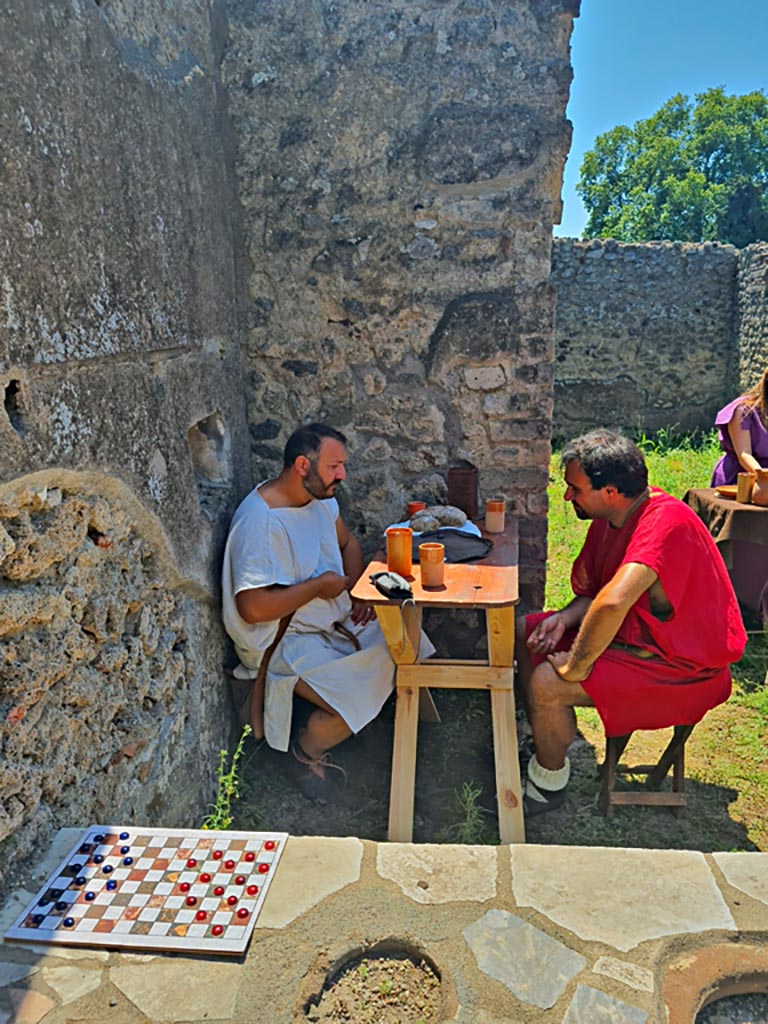 I.2.18 Pompeii. 8th June 2024.
Looking south across counter with actors playing part of customers. Photo courtesy of Giuseppe Ciaramella.
Historical reconstruction entitled L’altra Pompei prende vita (The other Pompeii comes to life).