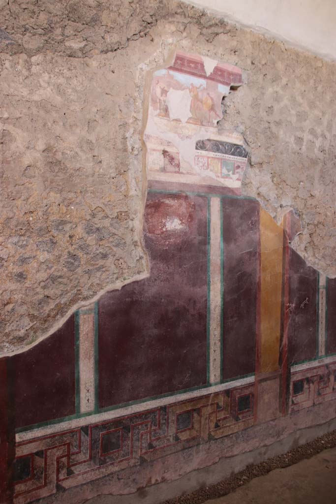 I.6.2 Pompeii. September 2019. Central section of west wall of west wing.
At the top is “the pestilence scene”, which was reconstructed from fragments.
Apollo can be seen with his bow, firing the plague arrows, above the rocks, in the upper left. 
The name of the god had been written on the painting in Greek letters (in white below the figure). 
People from Achaea pass in the foreground, including a man in a wagon drawn by a donkey, followed by man with a large round shield.
Photo courtesy of Klaus Heese.
