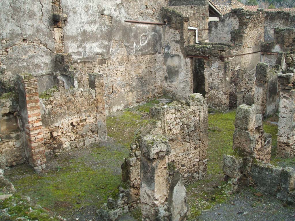 I.6.13 Pompeii. December 2004. Tablinum, atrium and east side looking south-east photo taken from rear of I.6.11. 
Behind the east wall of the tablinum, on left, would be the cubiculum (5) in NE corner of atrium.
Room 7 with doorway to corridor �e� is on the lower right, the corridor �e� is on the west side of the tablinum.
The remains of a lararium niche are on left of picture, in garden area behind tablinum.
According to Boyce �
�In the east wall of the garden is an arched niche (height 0.40, width 0.60, depth 0.27, height above the floor 1.30).
This was referred to in the report as �un modesto larario�.
See Boyce G. K., 1937. Corpus of the Lararia of Pompeii. Rome: MAAR 14. (p. 25, no.38) 
He quotes reference Not. Scavi, 1929, p.434.
