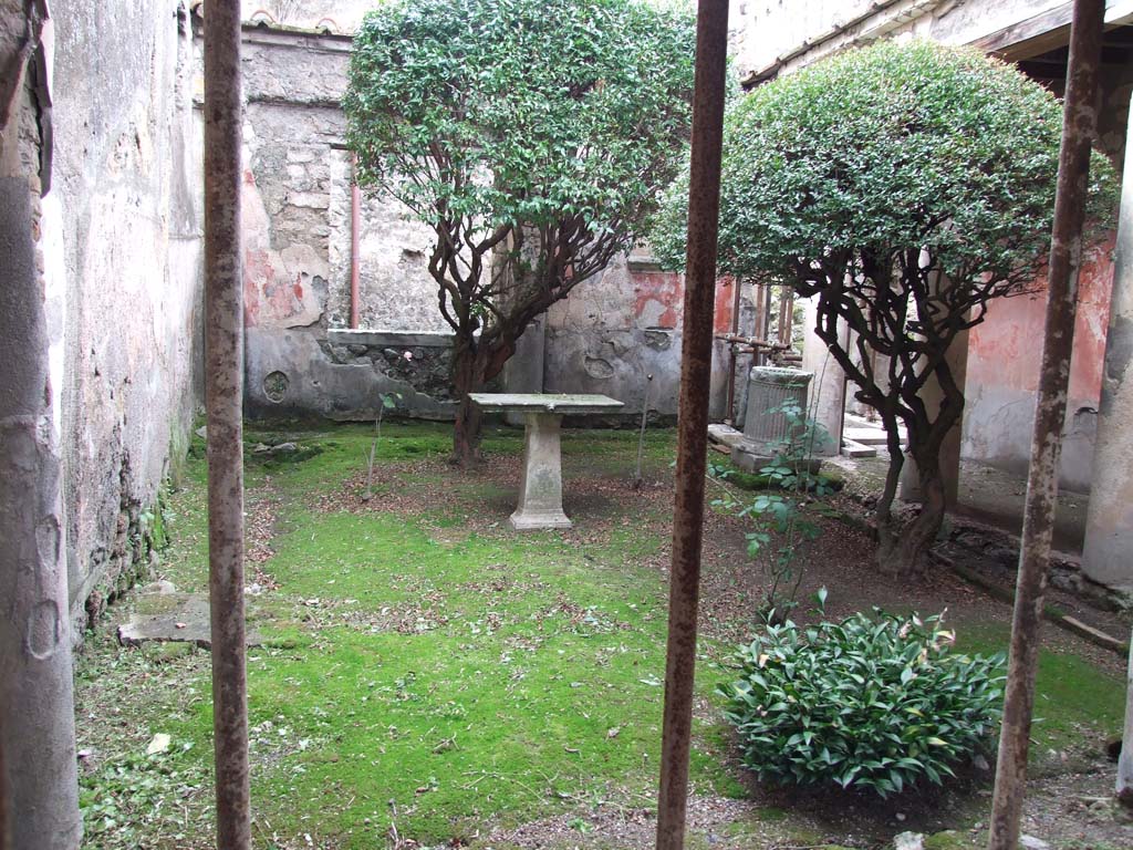 I.7.7 Pompeii. December 2006. Pseudoperistyle, looking west from east portico.
According to Jashemski, the garden was enclosed on the north and east by a portico supported by five columns and two engaged columns.
The room on the west side had a large window looking into the garden.
Maiuri pointed out that the large tree-root found against the south wall showed that the little garden had been well shaded.
The nail holes in the wall indicated that a vine had been carefully trained up the wall.
The tree-root cast can be seen half way up the garden next to the wall on the left (0.80 x o.80m at ground level).
There was a puteal over the cistern opening in the north-west part of the peristyle.
Another puteal was found in the garden.
The table (cartibulum) in the garden was decorated with lion heads on one side.
The small circular marble base probably held a statuette.
The arched niche with an aedicula façade on the west wall was a Lararium.
See Jashemski, W. F., 1993. The Gardens of Pompeii, Volume II: Appendices. New York: Caratzas. (p.37)