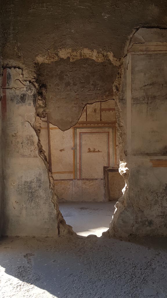 I.7.11 Pompeii. August 2023.
Looking towards north wall of the cubiculum on east side of atrium, through the hole in north wall from triclinium.
Photo courtesy of Maribel Velasco.