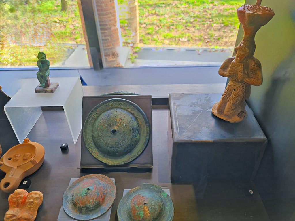 I.8.17 Pompeii. March 2024. No.7 – Bronze statuette of an actor (top left) (1st century AD). Photo courtesy of Giuseppe Ciaramella.
On display in cabinet in exhibition in Palaestra entitled – “L’altra Pompei, vite comuni all’ombra del Vesuvio”.
No.6 – Oil lamp with theatre masks (1st century AD), from I.9.9.
No.7 – Bronze statuette of an actor (1st century AD), from I.8.17.
No.8 – Bronze cymbals (1st century AD), provenance not known but from Pompeii.
No.9 - Oil lamp with Pan (1st century AD), from I.13.2.