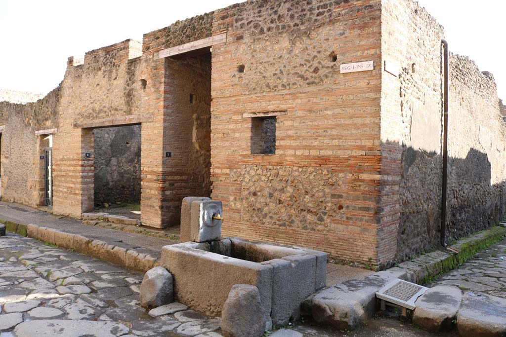 I.9.1 Pompeii, December 2018.
Looking south-east on Via dell’Abbondanza towards doorway at the rear of the fountain. Photo courtesy of Aude Durand.