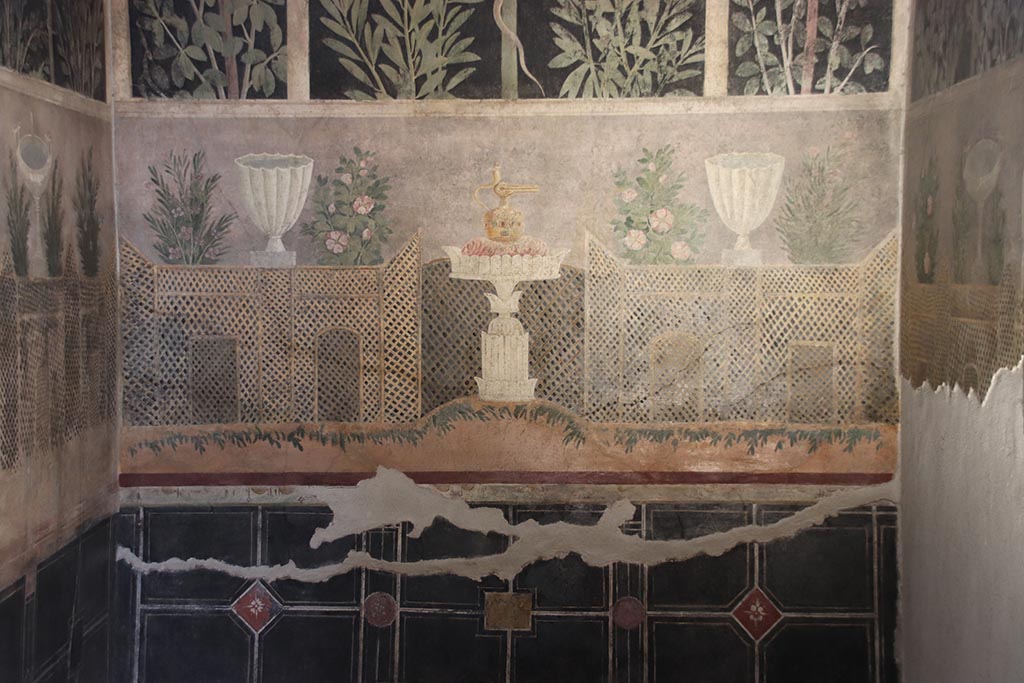 I.9.5 Pompeii. October 2024. Room 11, detail from lower east wall of cubiculum.
Garden painting with lattice fencing, white vases and table with Isis jug or jar. Photo courtesy of Klaus Heese