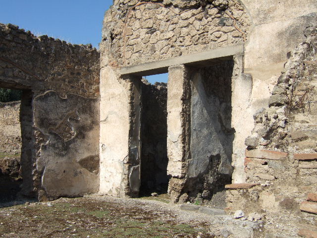 I.9.10 Pompeii. December 2006. South wall of atrium with doorways to three rooms.   On the left, the kitchen, in the middle at the rear a storeroom, and doorway on the right to a small room, possibly another storeroom.
