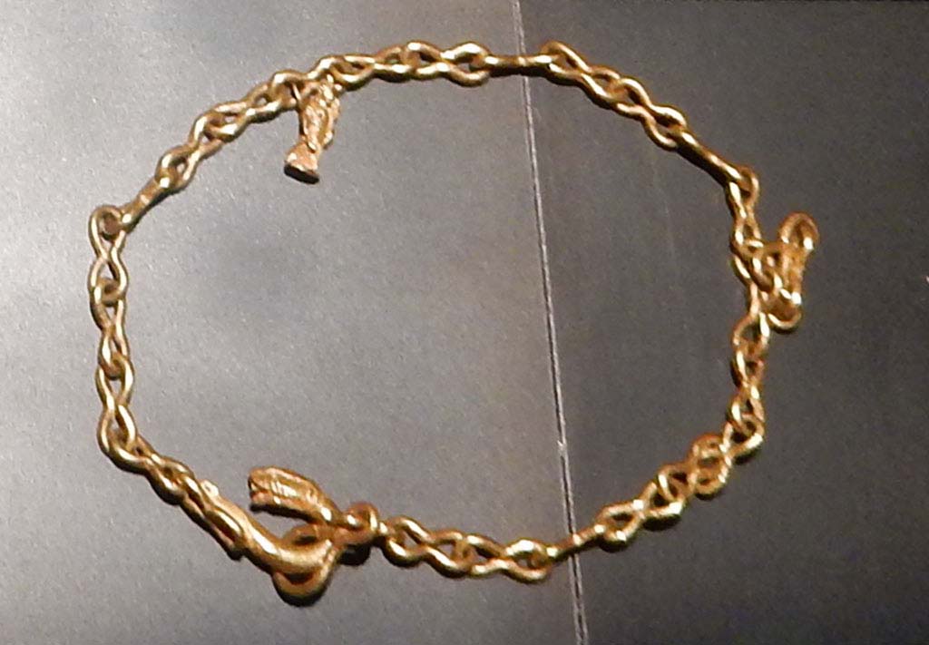 1.10.7 Pompeii, June 2019. 
Heavy gold chain with figure-of-eight links, snake head fastening and pendant featuring a statuette of Isis Fortuna, holding a rudder and cornucopia.
This was one of the jewels found in the atrium and in the tablinum.
On display in Palestra exhibition of jewellery entitled �Vanity, storie di gioielli dalle Cicladi a Pompei�, from 10th May 2019 to 5th August 2019.
SAP inventory number 5413. Photo courtesy of Buzz Ferebee.
See Guzzo, P.G. ed. (2003): Tales from an eruption � (Civale, A: The House of the Craftsman). Milan, Electa; (p.140-42)
