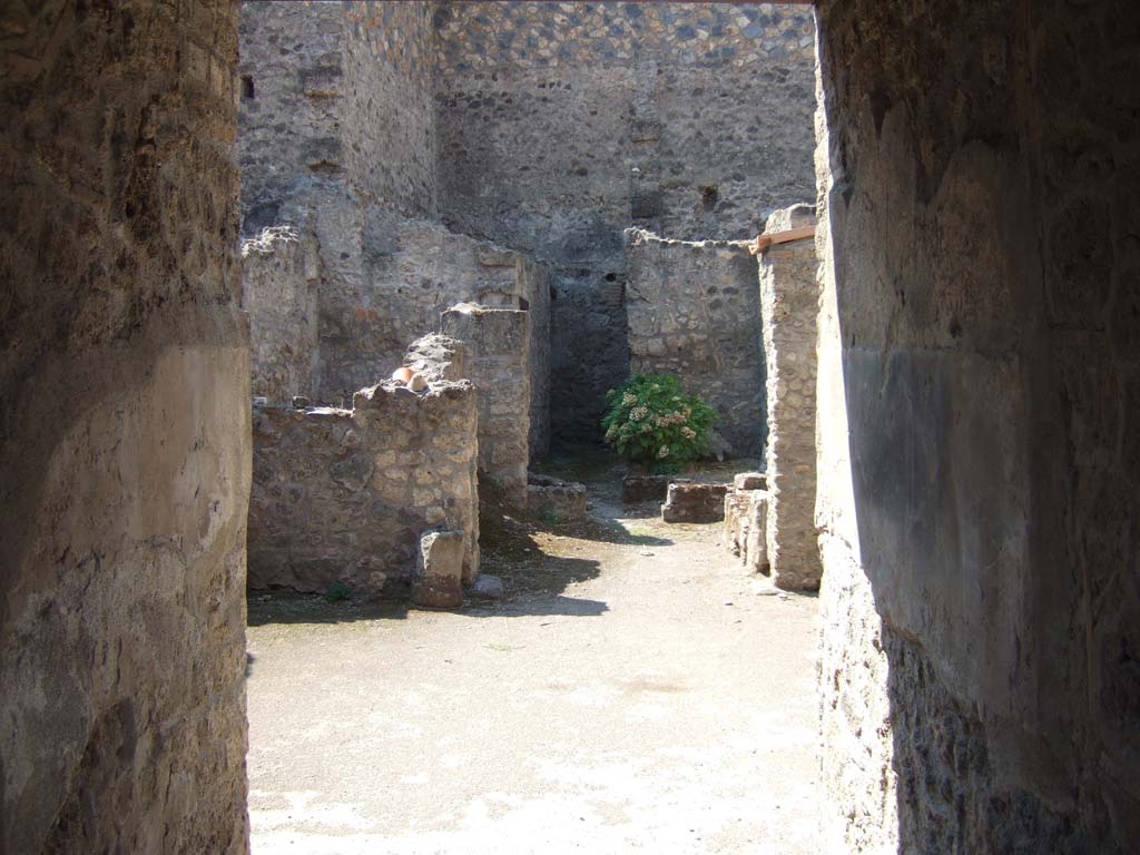 I.10.18 Pompeii. September 2005. Looking west from entrance fauces into atrium.
“The atrium, of an irregular shape, and paved with simple beaten-earth, had an impluvium of masonry (1.2m x 0.9m) faced with cocciopesto and embedded in its base were fragments of coloured marble, and this was placed almost in the middle of the atrium, but not in line with the entrance fauces.
A high black zoccolo, followed by the rest of the walls simply painted white, without any decorations, was the uniform aspect of the walls on all four sides.”