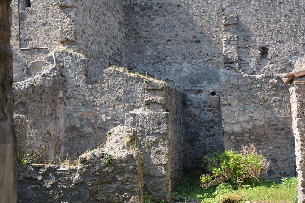 I.10.18 Pompeii. April 2017. Looking south-west from entrance fauces. Photo courtesy Adrian Hielscher.
“Along the south side (of the atrium 1) which was the wall next to the rustic quarters of the Casa del Menandro, a block of limestone was found, which would have been used as reinforcement for the wooden stairs that led up to the upper floor, of which one could see the outline in the plaster.
The “understairs”, closed towards the atrium by a wooden partition, had the two brick walls covered in simple white plaster.
On the west side of the atrium opened, respectively to the right and to the left,
- a large doorway opening into a room all open to the west (no.6) and defended only by a low wall, covered by canopy/roof,
- and with another room (no.7) of elongated trapezoidal shape, whose south wall, slanting, marks a tilt of the perimeter wall.
In the room to the right, (no.6) there is no trace of the original flat roof cover other than the two large holes of the lintel, there is, on the left side, a recess in the wall, to which a pile of lime had been attached and on the right side were the two limestone blocks, supporting an attached ladder. The flooring was of a simple floor of beaten material; the walls were covered with rustic white plaster, which did not have any decoration.
From here we pass by means of a door rather wide, but occupied in part by the circular mouth of the cistern, into a narrow and long area (no.8), uncovered, with a floor of cocciopesto, onto which poured the dripping of the roofs of this part of the house.
This area (no.8) gave access to the room described as the kitchen (no.9), and at the rear of no.8 was the latrine (no.10), which would have consisted of the usual seat with a recess in the wall for it.
On the back wall, two low masonry podiums are attached, the second of which was connected to a square base built in the corner.
Along the left side of the walkway (No.8), opened the kitchen, also rectangular and at a lower level than the walkway/yard. The hearth is in the SE corner opposite the entrance, with masonry bench (1.25 m x 0.86 x 0.86) and edges covered with bricks and tiles, on the south wall beyond the podium was the Lararium painting (0.35m x 1.10), preserved only for half of its length, on a white background framed by a red band.
In front of the kitchen was a very small rectangular uncovered area of a few square metres and bordered by a low wall, and in which poured the rainwater from the surrounding roofs.”
See Notizie degli Scavi, 1934, (p.341-4).
According to Allison –
The kitchen, room 9, had coarse plaster on its east and south walls and a tiled floor. On the south wall beside the masonry bench is the lararium painting (preserved for the height of I.8m).
The latrine, room 10, had coarsely plastered walls. The excavators recorded the remains of a wooden seat-plank in the wall, at the south end.
Its proximity to the kitchen suggests its additional use for general waste.
See Allison, P.M. (2006). The Insula of the Menander at Pompeii: Vol. III The finds, Clarendon Press, Oxford, (p.369-70).