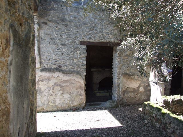 I.12.8 Pompeii. March 2009. Room 10, north-west corner of kitchen with lararium. On the north wall can just be seen some cloth, which has adhered to the lararium and damaged it.
It used to show one serpent approaching a round altar from the right. See Giacobello, F., 2008. Larari Pompeiani: Iconografia e culto dei Lari in ambito domestico. Milano: LED Edizioni. (p.152-3). According to Curtis, the lararium painting covering two walls above the oven in the kitchen was beautiful but badly-deteriorated. Painted on the north wall was a large single serpent near an altar. On the altar were sacrificial gifts, such as pine cones.
There may have been another scene beneath the serpent, but the wall was too badly damaged to verify this. See Curtis, R.I: The Garum shop at Pompeii, In Cronache Pompeiane, V,1979, (p.20-1)