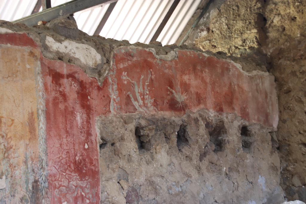 I.12.8 Pompeii. October 2022.
Peristyle 9, north wall at east end, detail of painted wall above holes for supports of ceiling above latrine 12. Photo courtesy of Klaus Heese.