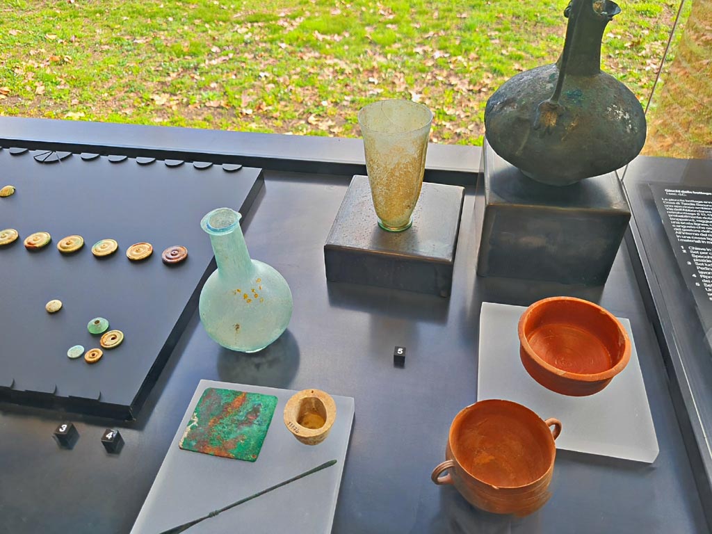 I.13.5 Pompeii. March 2024. Items found in a wooden crate in rear room. Photo courtesy of Giuseppe Ciaramella.
2. (lower centre). Female cosmetic set.
3. Game set.
4. Reproduction of a board for the game of the twelve signs.
5. Drinking set.
On display in exhibition in Palaestra entitled – “L’altra Pompei, vite comuni all’ombra del Vesuvio”.