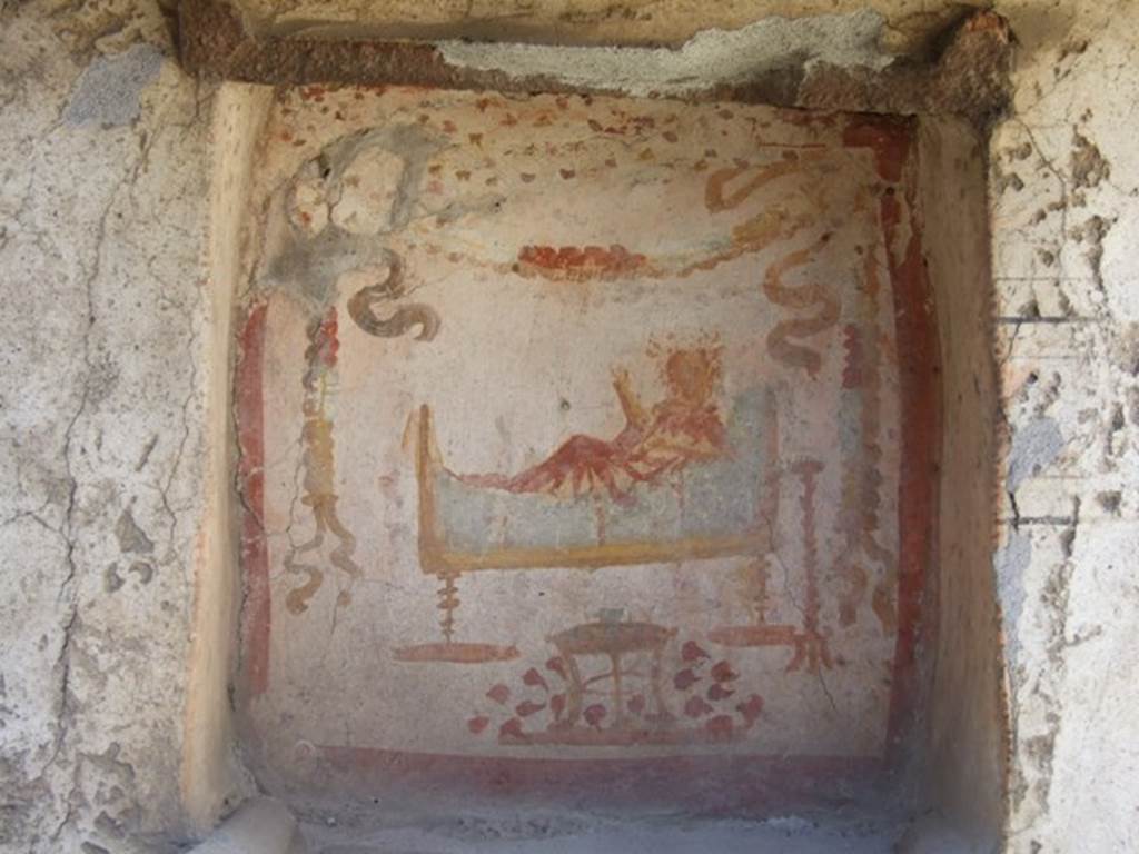 I.14.7 Pompeii. March 2009. West wall of garden area.  
Niche lararium with painting of a god in a long white robe lying on a couch.  
The right hand holds a branch and the left holds a patera.  
To the right is a golden candelabrum.  
At the front is a three legged table with a bowl of fruit.  Above is a garland.
See Fr�hlich, T., 1991. Lararien und Fassadenbilder in den Vesuvst�dten. Mainz: von Zabern. (L34, T:29,3)
