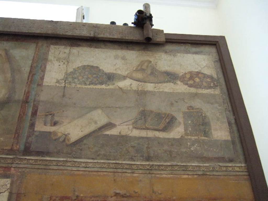 II.4.10 Pompeii. Detail of upper wall from tablinum of Praedia di Giulia Felice (Julia Felix).
Painting showing two piles of coins, a bag of money, pen and ink, a scroll, double and single wax tablets and writing instruments.
Now in Naples Archaeological Museum. Part of inventory number 8598.
According to Andersson, although heaps of money are depicted above wax tablets on the legendary wall painting from the property of Julia Felix (II 4.1 – 12), archeologically speaking, money has never been found near wax tablets.
See Andersson E. B., 2018. The Economic Centre of Pompeii Revealed by Roman Cash Keeping, in Archaeology and Economy in the Ancient World, p. 160 and fig. 4.