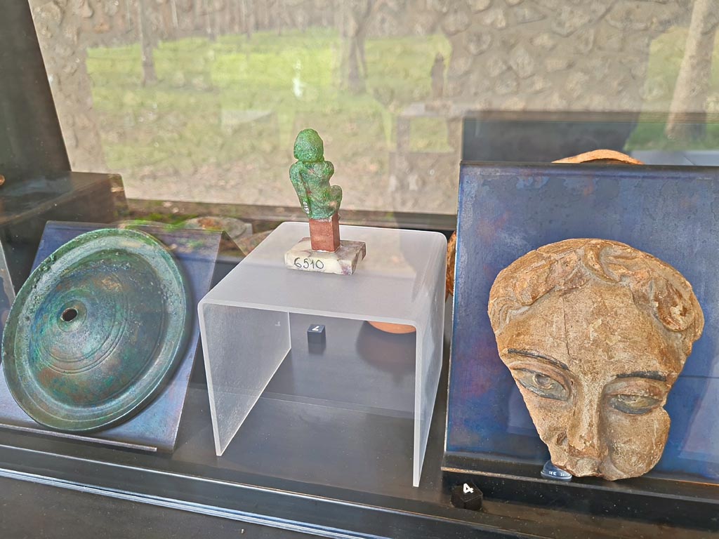 II.7.9 Pompeii. Palaestra. Rear of above cabinet, on display in exhibition in Palaestra entitled – “L’altra Pompei, vite comuni all’ombra del Vesuvio”. March 2024.
On left, No.8 – Bronze cymbals from Pompeii.
In centre, rear of No.7 - Bronze statuette of an actor from I.8.17.
On right, No.4 – one of two Terracotta theatre masks from Pompeii. 
Photo courtesy of Giuseppe Ciaramella.
