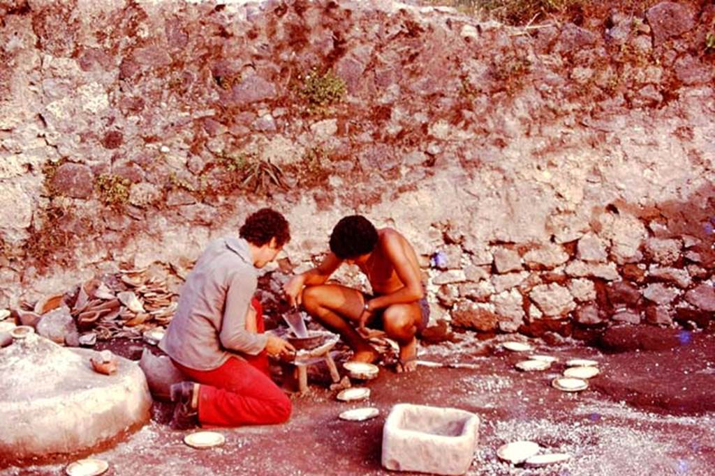 III.7 Pompeii. 1976. Two of Wilhelmina�s helpers, Raffaele and Renato, kneeling down and pretending to cook on the brazier. Photo by Stanley A. Jashemski.   
Source: The Wilhelmina and Stanley A. Jashemski archive in the University of Maryland Library, Special Collections (See collection page) and made available under the Creative Commons Attribution-Non Commercial License v.4. See Licence and use details. J76f0478
