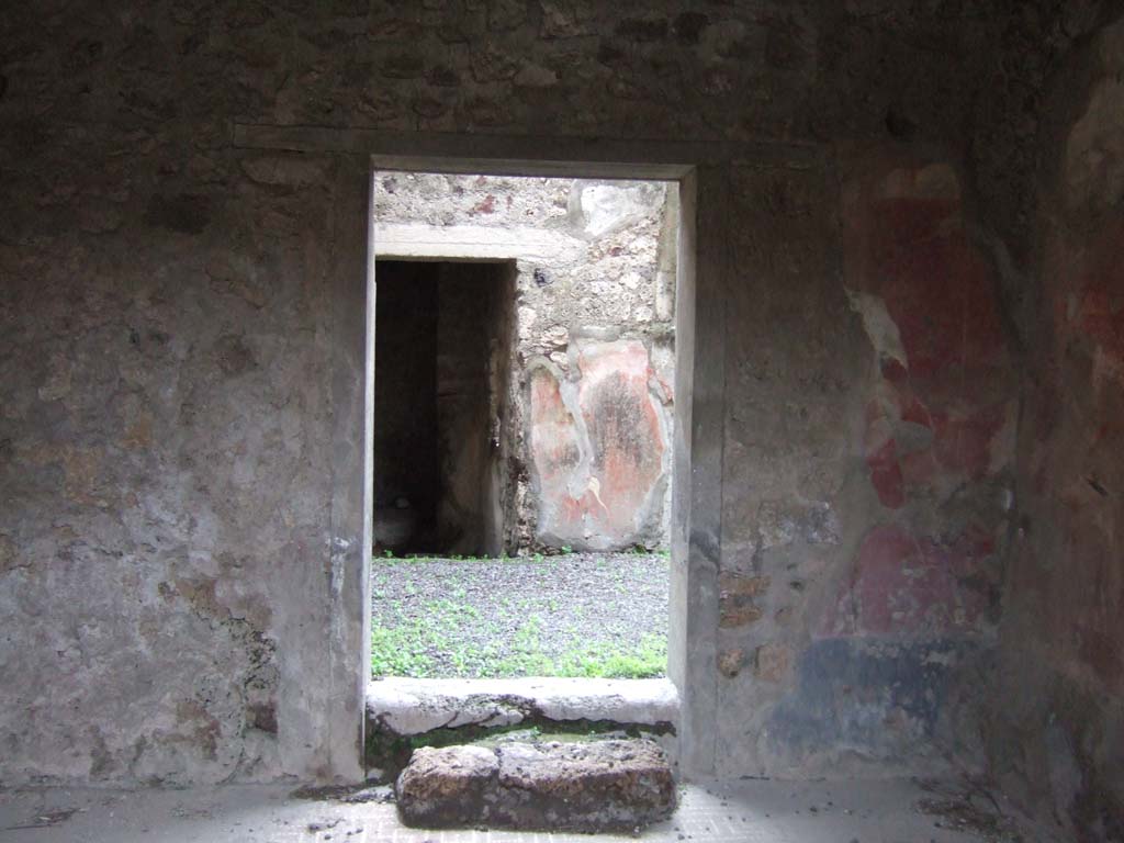 V.2.h Pompeii. December 2005. South wall of room ‘f’ the tablinum, with doorway to rear.
Opposite the entrance fauces was the tablinum, situated between the corridor and the cubiculum.
The tablinum had flooring of signinum and walls with a red background, with black dado and white frieze.
The decoration had nearly all fallen from the south wall.
In the south wall was a block of limestone, which served instead of a step to the doorway which opened out into the small garden ‘h’.
In the central panels of the east and west walls were the circular paintings with heads of youths with crowns of foliage.
These are now found in the Naples Archaeological Museum, (see NdS, 1892, p.28)
Another two medallions with heads were painted on the south wall near to the above-mentioned doorway, as could be seen by the remains of a medallion on the pilaster to the right, in which part of the head was visible.
In the side panels were medallions with landscapes.
Also, here and there on the walls of the tablinum could be seen traces of fire.
See Notizie degli Scavi di Antichità, 1896, (p.422) which refers to tablinum ‘b’, corridor ‘c’, cubiculum ‘d’ and the garden ‘f’.