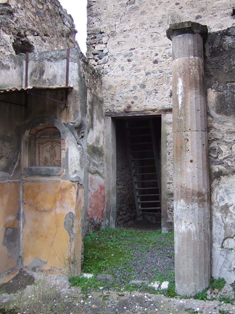 V.2.h Pompeii. December 2005.
Looking north to doorway from walkway ‘k’, across area ‘h’, to room ‘e’, the corridor, with wooden reconstructed stairs to the upper cenacolo.
According to NdS, corridor ‘e’ had a threshold of travertine and walls covered with a rustic white plaster.
In the north-west corner of room ‘e’ was a low masonry block, probably the beginning of an ascending stairway.
At the south end of the corridor was a doorway (seen above) leading into area ‘h’, which also had doorways to the tablinum ‘f’, to room ‘i’ a cubiculum, to room ‘l’ triclinium, and doorway to walkway ‘k’ (above) leading to the garden, room ‘n’.
The small garden ‘n’ was preceded by a walkway ‘k’ protected by a roof, which projected from the roof, which covered room ‘h’.
This walkway had a floor of flagstones, littered with chunks or flakes of marble, and did not show any other decoration other than a high yellow dado on the west wall and in the north-west corner.
See Notizie degli Scavi di Antichità, 1896, (p.423) which refers to walkway ‘h’, across area ‘f’, to corridor ‘c’, with wooden stairs, cubiculum ‘i’, triclinium ’g’, garden ‘l’.
In the north-west corner of walkway ‘h’, on the north side of the garden, was a lararium niche and column.
According to Boyce, in the garden was found a cylindrical altar of terracotta, around which a serpent coiled, its head raised above the top.
See Boyce G. K., 1937. Corpus of the Lararia of Pompeii. Rome: MAAR 14. (p.36, note 1).