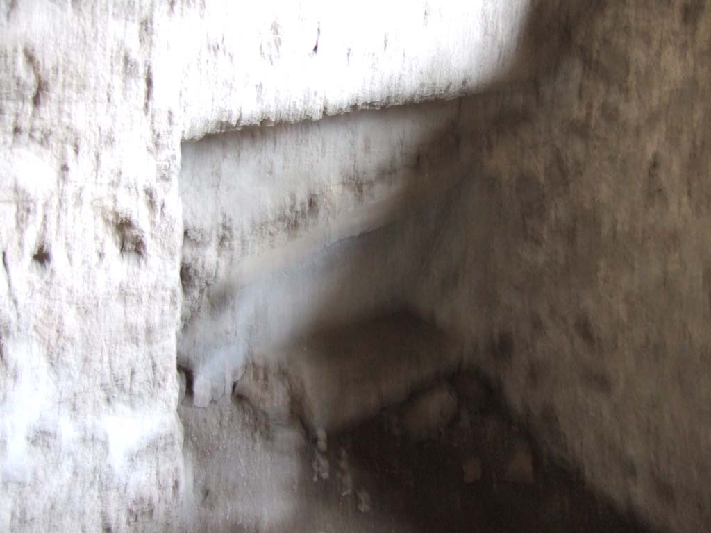 V.2.h Pompeii. December 2005. Kitchen ‘p’, recess in north-west corner.
According to Spano, a square window with preserved grating was found in the north wall.
Along the north wall, but perhaps at night only, may have been put a small bed.
In the west part of the north wall can be seen the characteristic hollowed recess destined to contain one of the ends of the bed.
See Spano in Notizie degli Scavi di Antichità, 1910, p.330 where the kitchen is referred to as ‘d’.
According to NdS, (1896), the west side (on the left) of the atrium was devoid of rooms.
On the east side, there was one small area with the possible clue of a staircase ascending to the rooms above the entrance fauces and the two adjacent rooms.
See Notizie degli Scavi di Antichità, 1896, (p.422).
In NdS, (1910), further excavation had discovered a doorway to the kitchen on the east side of the atrium.
According to the newer discovery, it was then thought that the room above the cubiculum on the right of the fauces was accessible from above a room in the adjoining house.
The kitchen and the room from the house next door would have been in communication in ancient times.
In the left half of the east wall of the kitchen, a bricked-up wall/doorway could be seen.
A latrine was then constructed in front of the new bricked up wall, with the hearth on its right.
See Notizie degli Scavi di Antichità, 1910, (p.329-330) where the cubiculum on the west is referred to as ‘c’ and the east one as ‘b’.