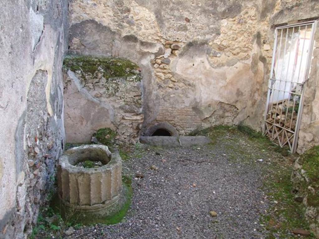 V.2.i Pompeii. December 2007. Room 11. Kitchen. Wall at south end near the caldarium showing a hole in the floor, used to heat the bath rooms. On the left in the south east corner are the remains of a masonry foundation, possibly to support the lead vessel in which water was kept for the bath. The stone puteal in the form of a Doric column does not cover a cistern mouth. See Allison, P. M. Pompeian Households: An online companion. http://www.stoa.org/projects/ph/rooms?houseid=16#293 (room s). On the right on the west wall is the door (now gated) to the latrine.