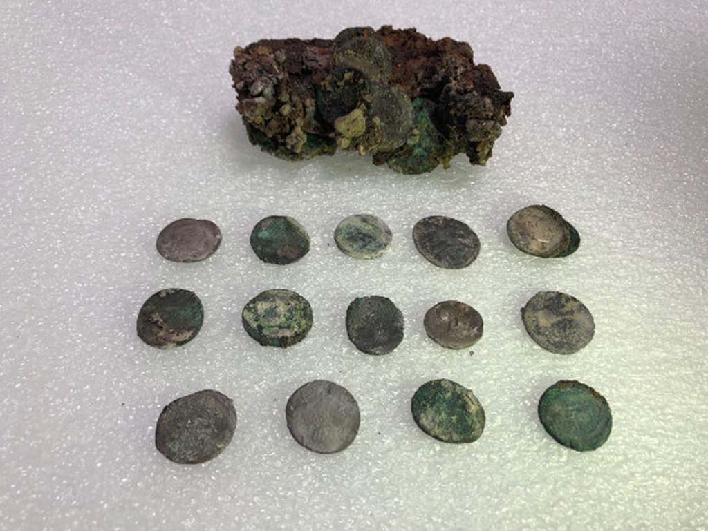 Regio V Pompeii. 2018. Leather pouch containing coins found under Pompeii skeleton in the Vicolo dei Balconi.
At first examination of the money found with skeleton of victim there would seem to be at least 20 silver denarii and two bronze asses for a nominal value of eighty sesterces and a half.
Such a quantity of coins could at that time ensure the maintenance of a three-person family for 14, 16 days.
The coins have very varied chronology.
It was possible to examine 15 coins, for the main part Republican, starting from the Mid-second century B.C.
One of the later Republican coins is a legionary denarius of Mark Antony, common in Pompeii, with the indication of the XXI Legion.
Among the few Imperial coins identified, a probable denarius of Octavian and two denarii of Vespasian.
Borsa di cuoio contenente monete trovate sotto lo scheletro di Pompei nel Vicolo dei Balconi.
Al primo esame delle monete trovato con lo scheletro della vittima sembrerebbero esserci almeno 20 denari d'argento e due as di bronzo per un valore nominale di ottanta sesterzi e mezzo.
Una tale quantità di monete potrebbe quindi garantire il mantenimento di una famiglia di tre persone per 14, 16 giorni.
Le monete hanno una cronologia molto varia.
Fu possibile esaminare 15 monete, per lo più repubblicane, a partire dalla metà del II secolo a.C.
Una delle monete repubblicane più tardi è un denario legionario di Marco Antonio, comune a Pompei, con l'indicazione della XXI Legione.
Tra le poche monete imperiali identificate, un probabile denario di Ottaviano e due denari di Vespasiano.
Photograph © Parco Archeologico di Pompei.