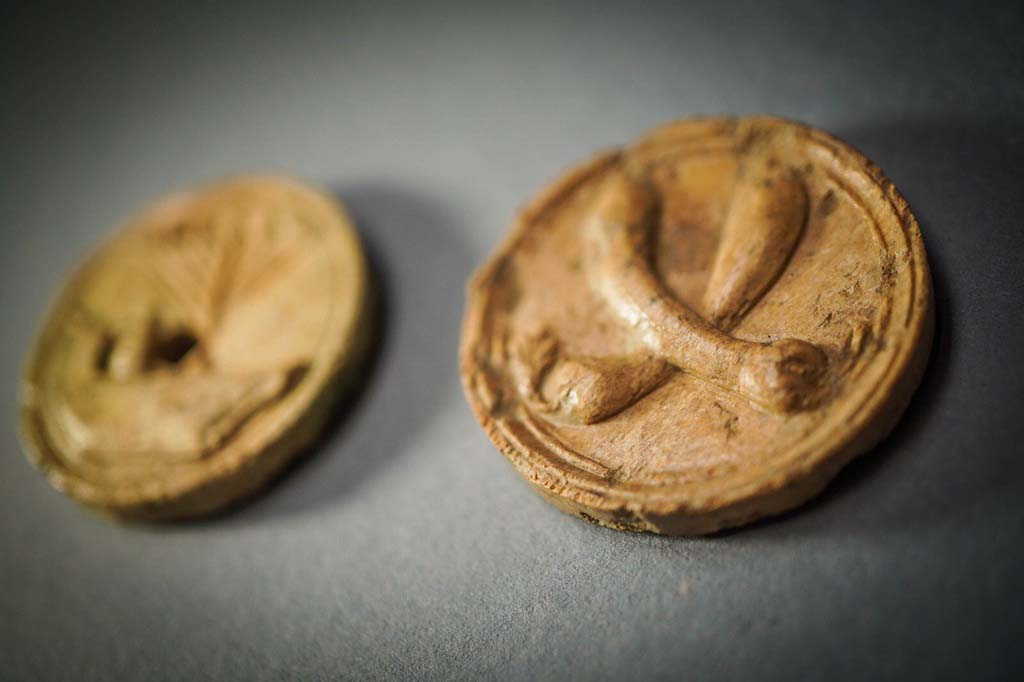 V.3 Pompeii. Casa del Giardino. August 2019. Two bone buttons. On the one in the foreground there are two courgettes.

Due bottoni in osso. Su quello in primo piano ci sono due zucchine.

Photograph © Cesare Abbate/ANSA courtesy Parco Archeologico di Pompei.
