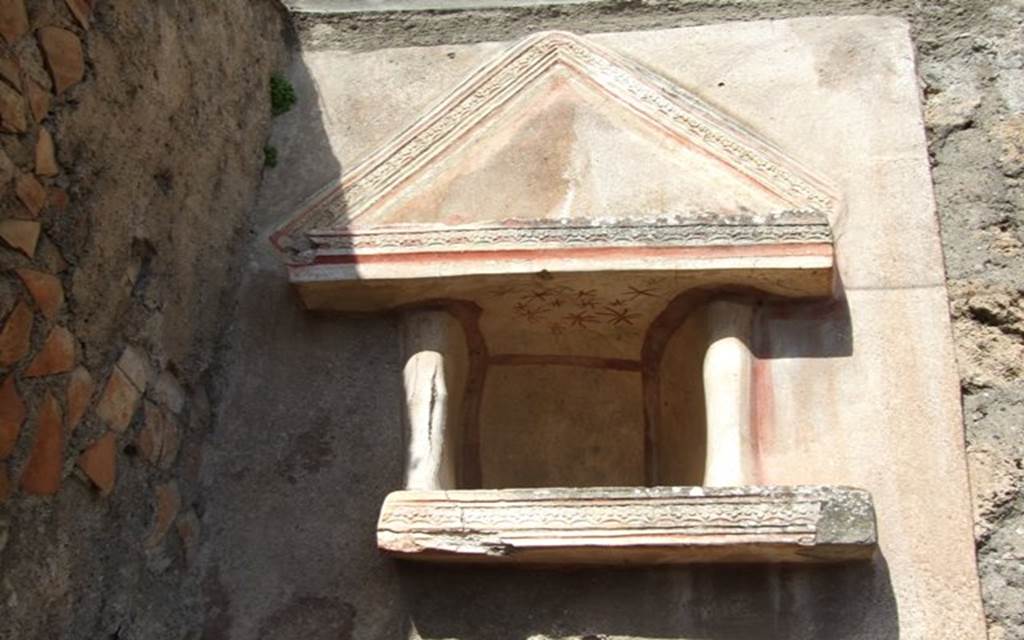 V.4.9 Pompeii. March 2009. Lararium niche. According to Boyce, this Lararium was on a special panel of rough white stucco, and was adorned with an aedicula fa�ade. Beneath the niche was a heavy shelf with two columns resting on it, framing either side of the niche. The interior of the niche was white and outlined with red stripes. On the ceiling of the niche there were red and green star decorations. Within the niche were found the following figures � A bronze bust of Minerva, wearing the aegis and helmet. She was leaning backwards in a strange manner upon a bronze plate fitted with a sort of handle at the back.
A roughly worked alabaster figure of Venus wearing a crown, beside her to the left stands a small figure clad in a long garment. Venus seems to held her left hand around the smaller figure, while the latter placed her right hand upon the head of the goddess. This group stood upon a marble-covered base behind the bust of Minerva. A small standing male figure of ivory. Sogliano thought the figure was Venus, Mau thought it was definitely male.
Also found in the niche were two small rectangular terracotta altars and two terracotta plates. See Notizie degli Scavi di Antichit�, 1899,pp.103. See Boyce G. K., 1937. Corpus of the Lararia of Pompeii. Rome: MAAR 14. (p.41, no.123, Pl.7,1).